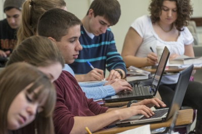 Students taking notes on paper and laptops in a U.S. classroom